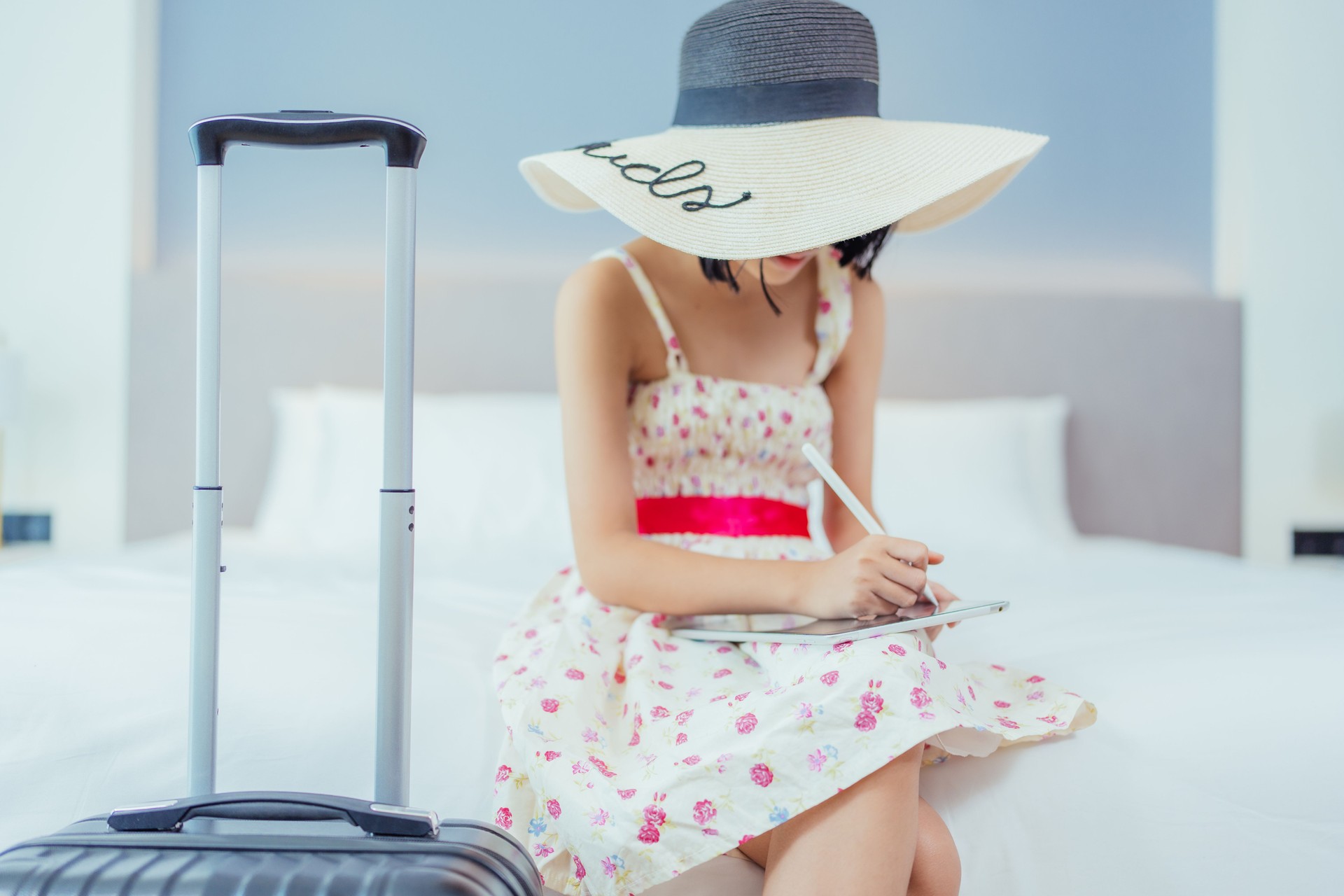 Dressed in her hat, glasses, and dress, a young Asian woman, a tourist, arrives at a luxury hotel with her suitcase, prepared to celebrate and indulge in some summer relaxation.